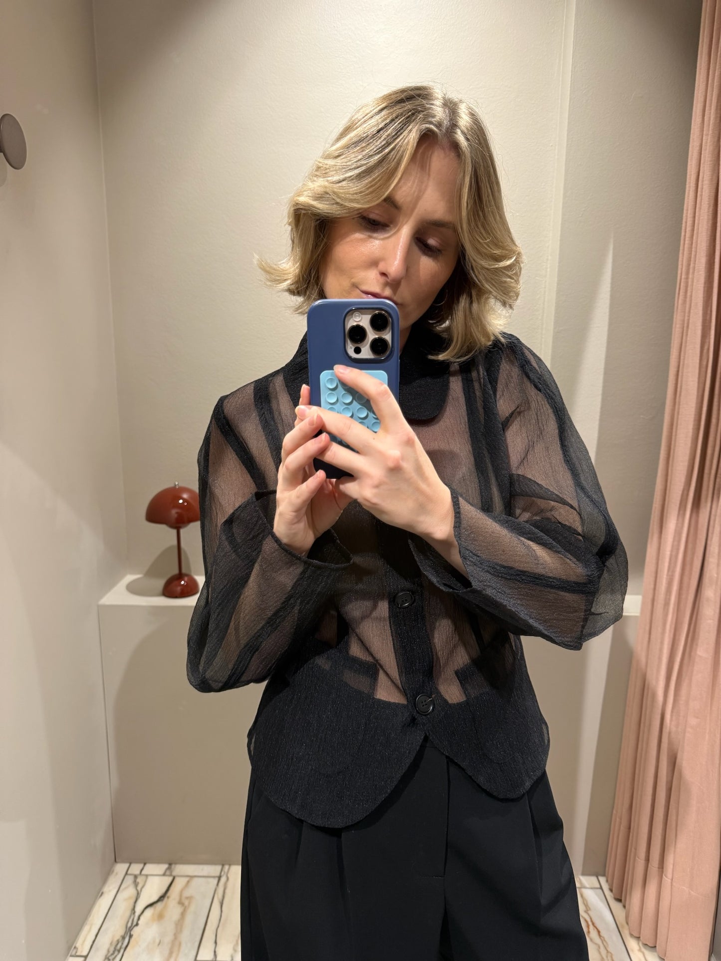 Frau macht Spiegelselfie, sie trägt schwarze Hose und schwarze transparente Bluse.
