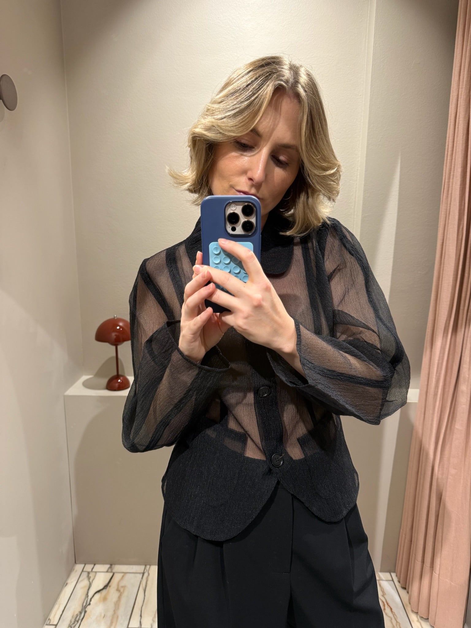 Frau macht Spiegelselfie, sie trägt schwarze Hose und schwarze transparente Bluse.