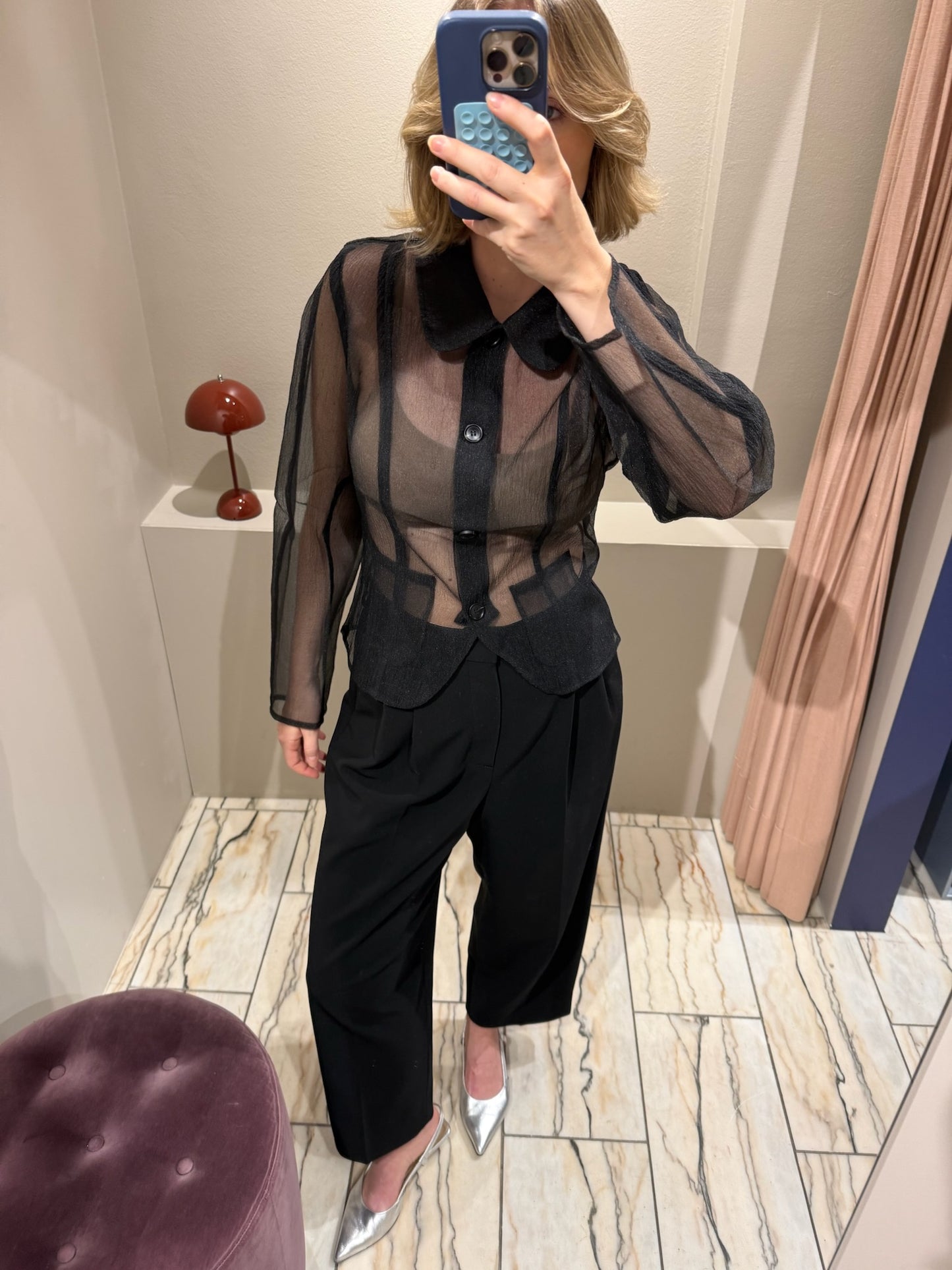 Frau macht Spiegelselfie, sie trägt schwarze Hose und schwarze transparente Bluse.