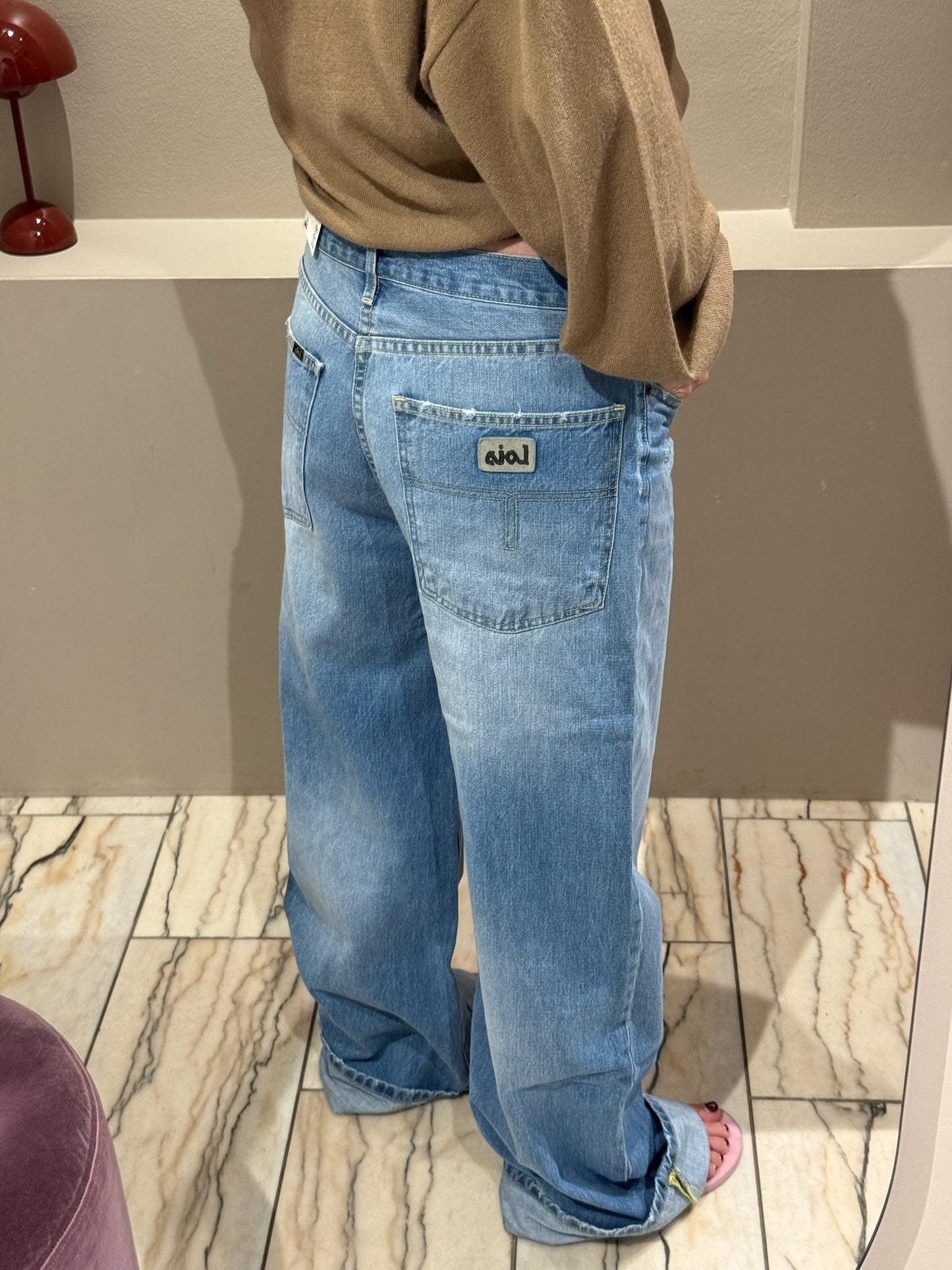 Frau macht Spiegelselfie, sie trägt eine Weite hellblaue Jeans und einen Camelfarbenden V-Neck Strick. Das Fote zeigt die Jeans von hinten, man sieht die taschen am Po.