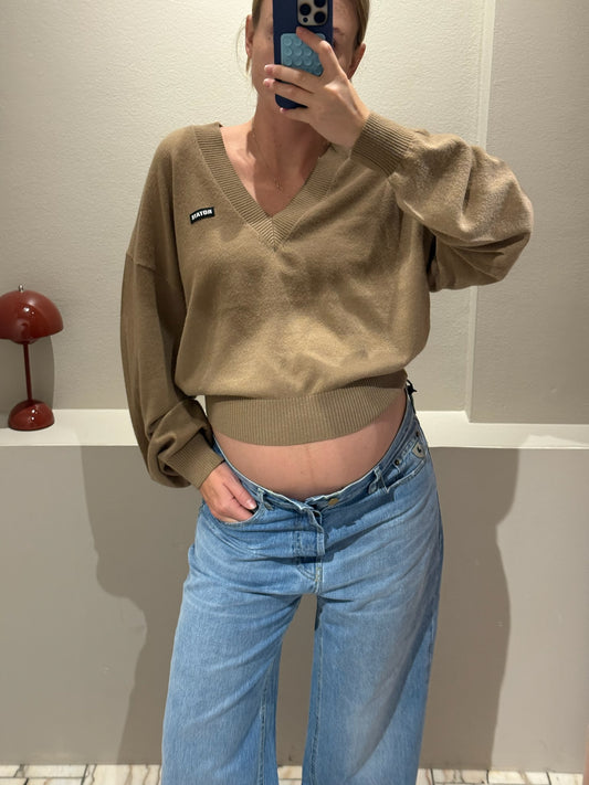 Frau macht Spiegelselfie, sie trägt eine Weite hellblaue Jeans und einen Camelfarbenden V-Neck Strick.
