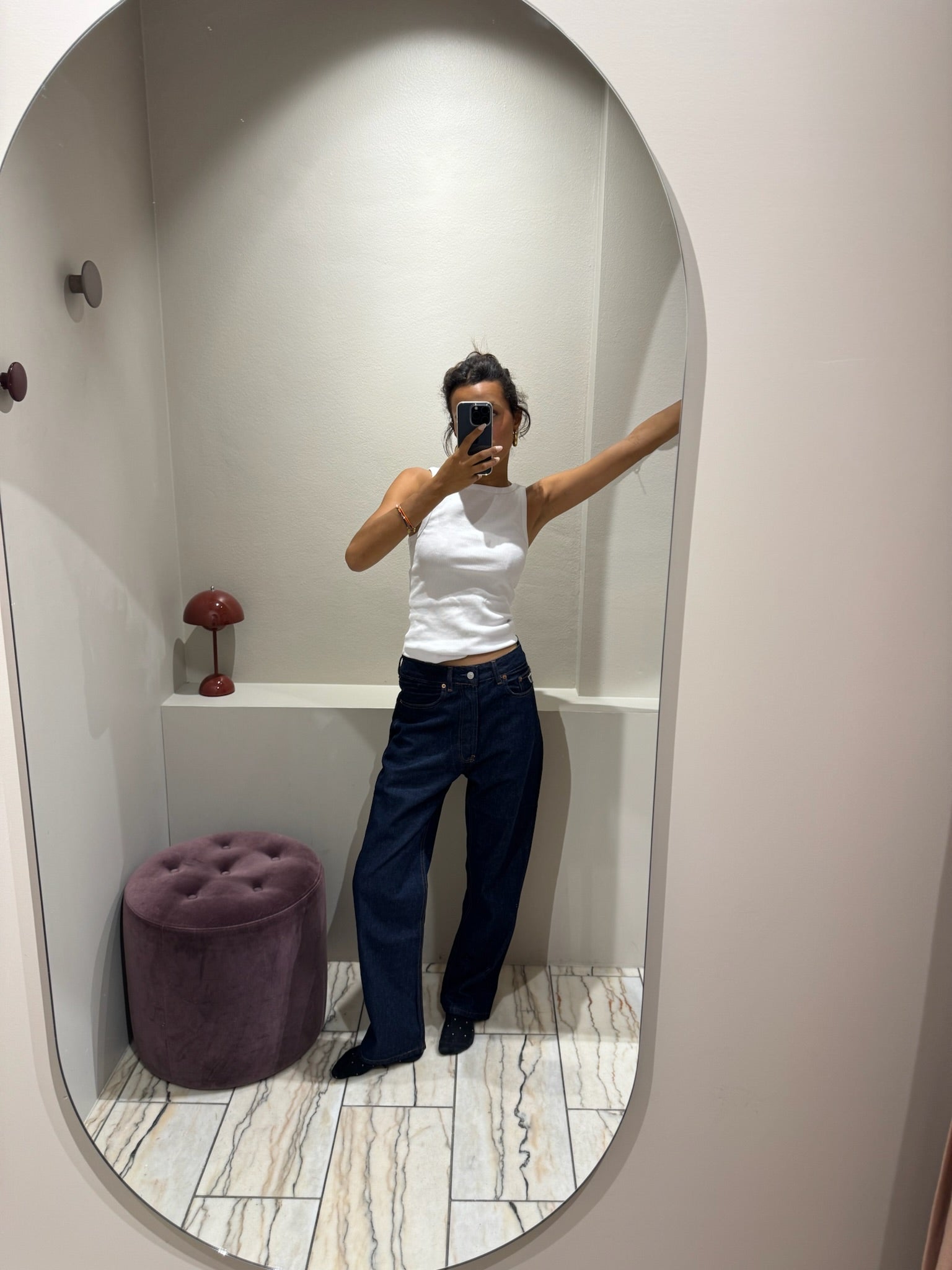Frau im Spiegel, sie trägt eine dunkleblaue lässige Jeans und ein weißes Top.