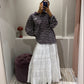 Eine Frau macht ein Spiegel Selfie, sie trägt einen weißen Rock mit horizontalen Lochstick-Streifen und Rüschensaum. Der rock ist sehr romantisch und fällt locker. Dazu styled sie ein oversized Polo und Cowboyboots.
