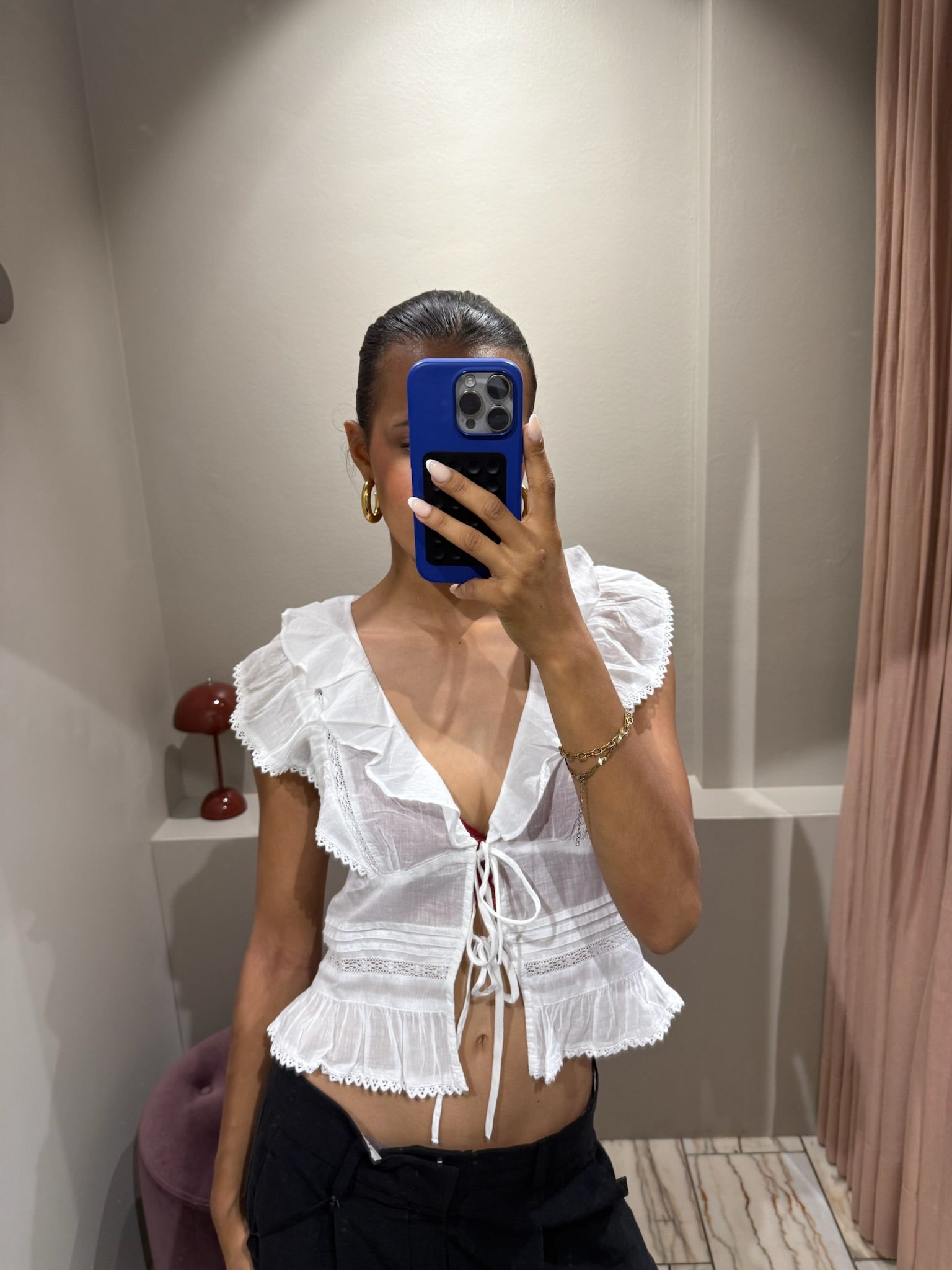 Eine Frau macht ein Spiegel Selfie, sie trägt eine weiße Kurzarmbluse mit Voilants und sie ist leicht transparent.