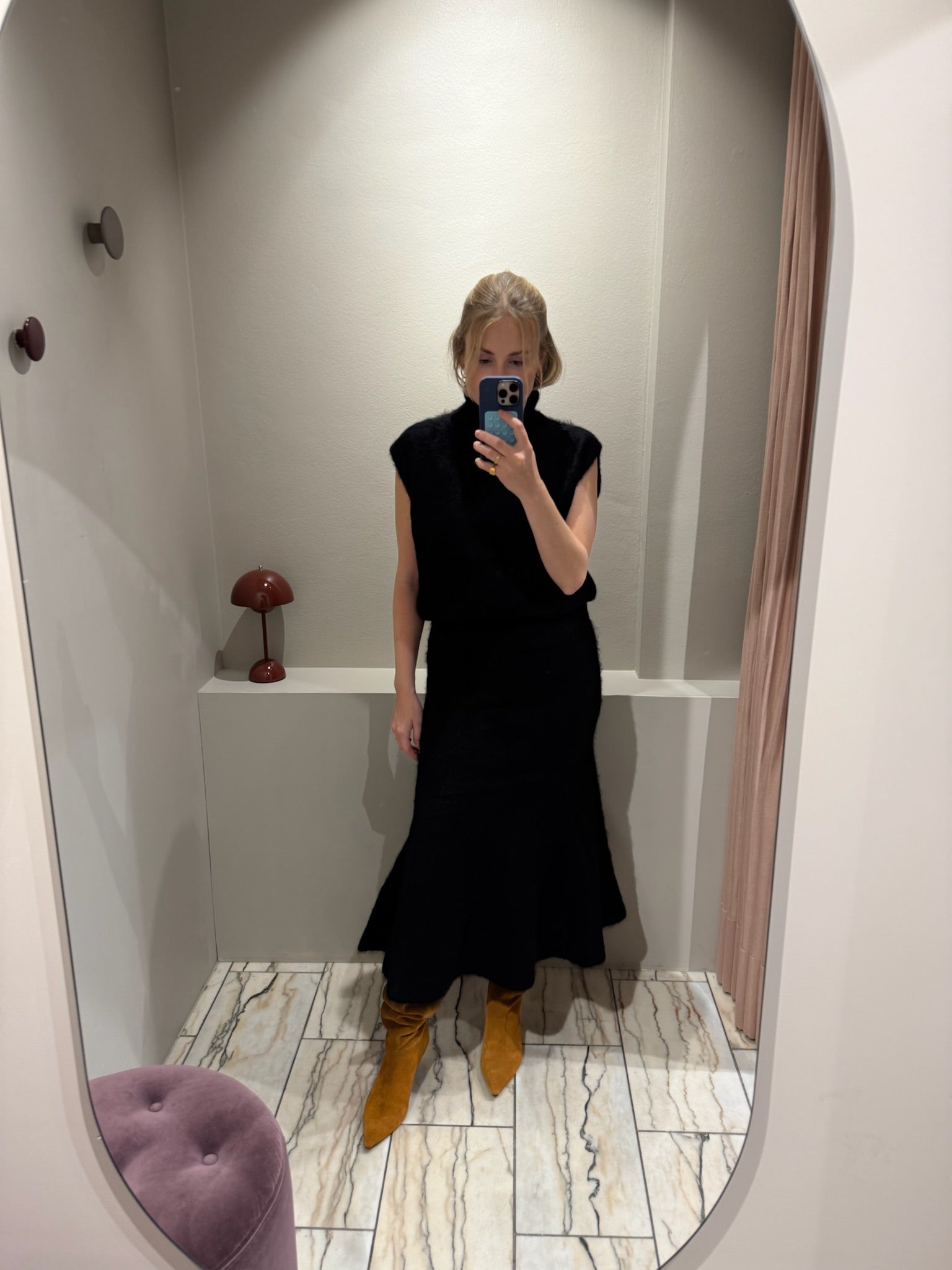 Frau macht ein Spiegelselfie, sie trägt ein set aus Strickrock und Pullunder in schwarz. Dazu kombiniert sie Wildlederboots.