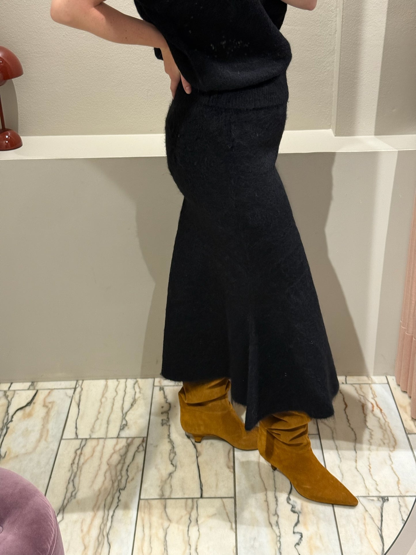 Frau macht ein Spiegelselfie, sie trägt ein set aus Strickrock und Pullunder in schwarz. Dazu kombiniert sie Wildlederboots.