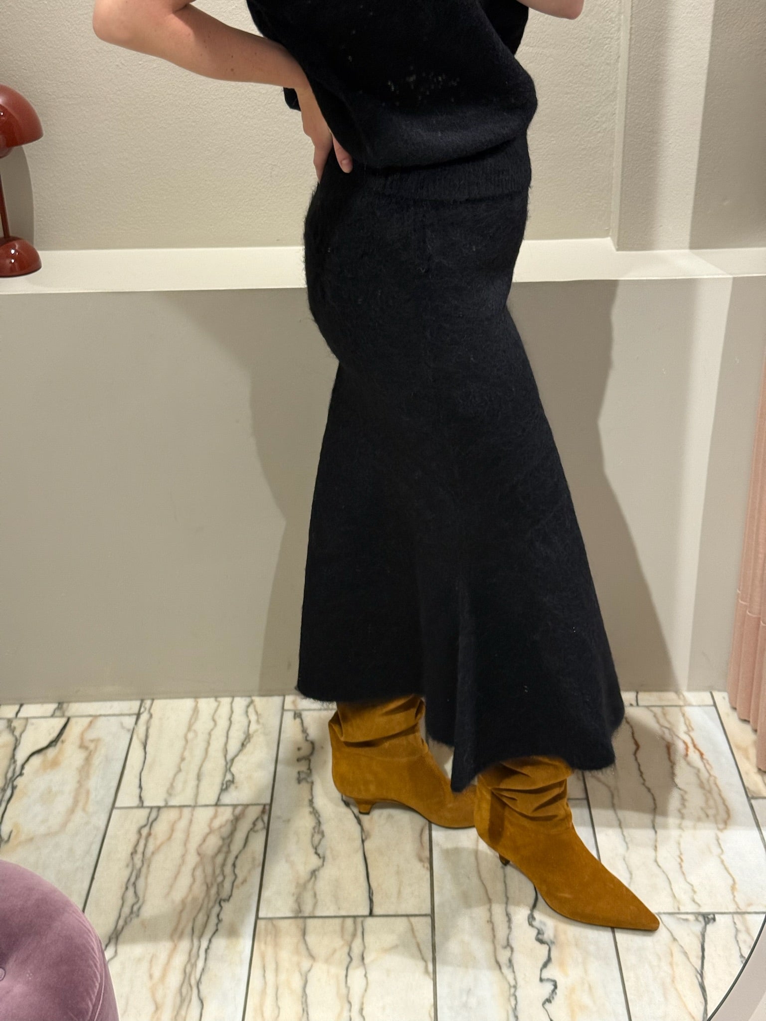 Frau macht ein Spiegelselfie, sie trägt ein set aus Strickrock und Pullunder in schwarz. Dazu kombiniert sie Wildlederboots.