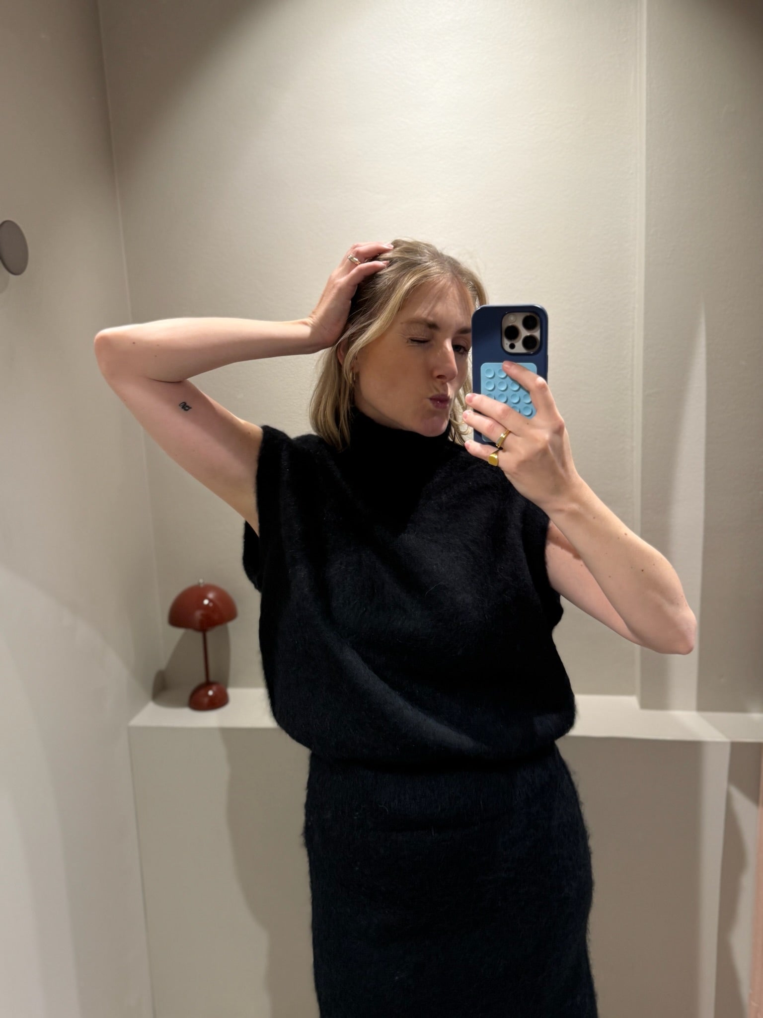 rau macht Spiegelselfie, sie trägt eine schwarze weite Hose und einen schwarzen Turtleneck-Pullunder.