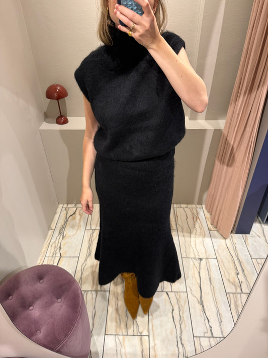Frau macht ein Spiegelselfie, sie trägt ein set aus Strickrock und Pullunder in schwarz. Dazu kombiniert sie Wildlederboots.