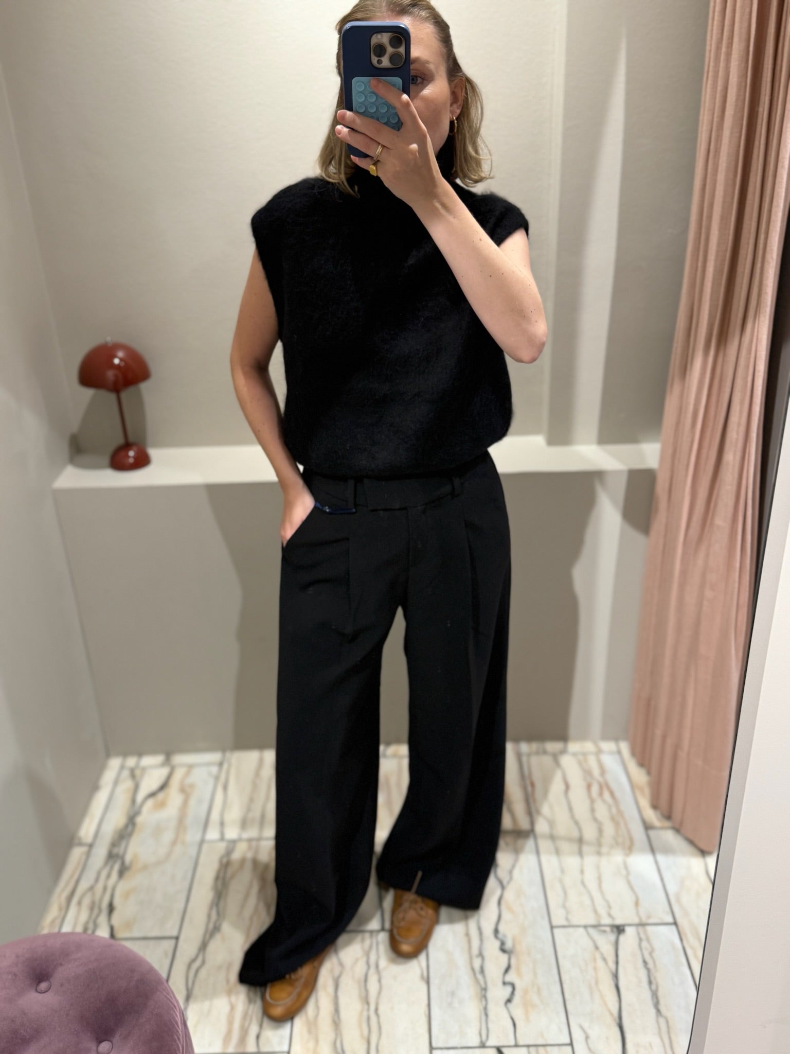 Frau macht Spiegelselfie, sie trägt eine schwarze weite Hose und einen schwarzen Turtleneck-Pullunder.