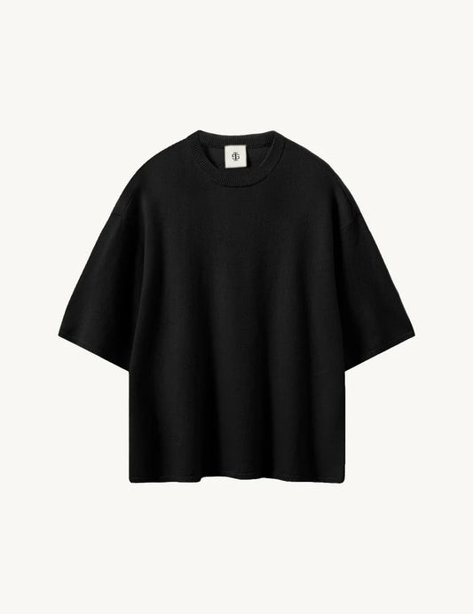 Kastiges schwarzes Strick Tee vor weißem Hintergrund.