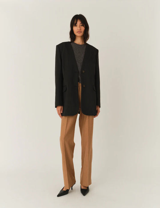 Frau vor weißem Hintergrund, sie trägt eine beige Hose und graues top Darüber einen Blazer ohne Reviere mit Nadelstreifen in dunkelgrau.